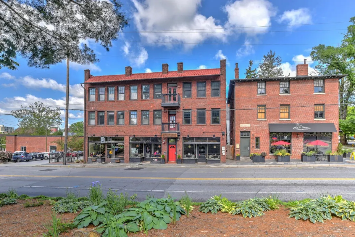 This image captures a lively exterior street scene featuring a red door, balcony, and storefronts. There’s visible pedestrian activity, suggesting people shopping, dining, and enjoying the vibrant atmosphere of the area. The festive decorations hint at seasonal or cultural events, showcasing the neighborhood's dynamic character.