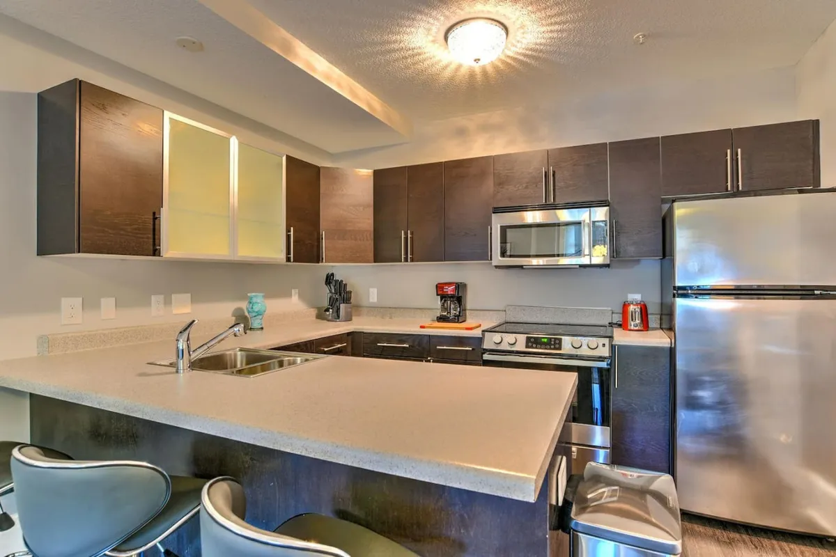 A stylish kitchen island is the focal point, surrounded by gleaming stainless steel appliances and accented by striking light fixtures. The space is designed for both culinary creativity and easy entertaining, offering an inviting nook for breakfasts or intimate dinners.