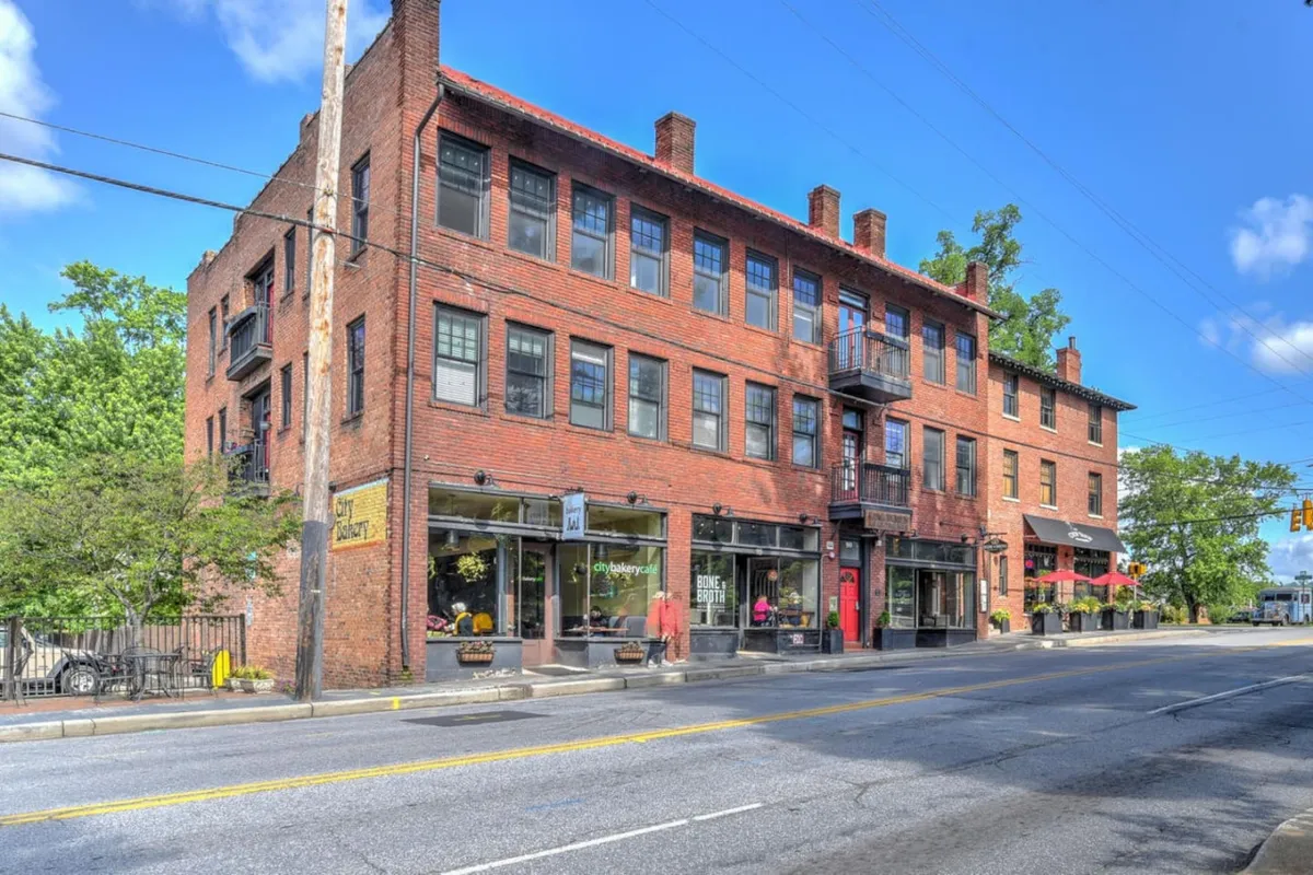 This exterior shot highlights the historic brick architecture of the King James Building, large display windows, balconies, and an outdoor seating area. The setting is lively, with the potential for shopping and dining just steps away.